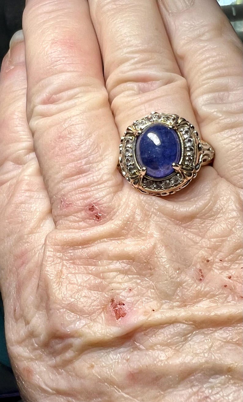May include: A gold ring with a large blue oval gemstone surrounded by smaller clear gemstones.