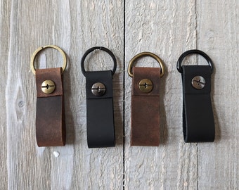 May include: Four leather keychains with different colored leather and metal rings. The keychains are brown, black, brown, and black.
