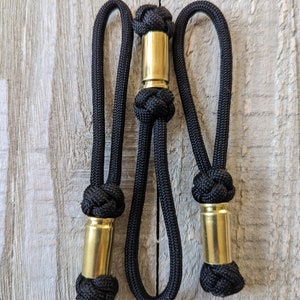 May include: A black paracord lanyard with three brass bullet casings woven into the cord.