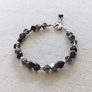 May include: A silver bracelet with dark purple and gray faceted beads. The bracelet has a silver clasp.