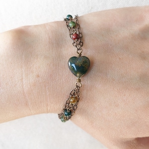 May include: A multi-strand bracelet with a green heart-shaped stone charm and small round beads in shades of green, brown, and red.
