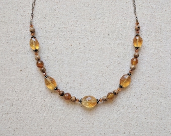 May include: A gold and brown beaded necklace with a silver chain. The necklace features oval-shaped beads and smaller round beads.