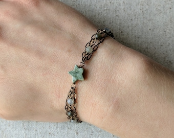 May include: A multi-strand bracelet with a star-shaped green stone charm. The bracelet is made of brown chain and small, round, gray and white beads.