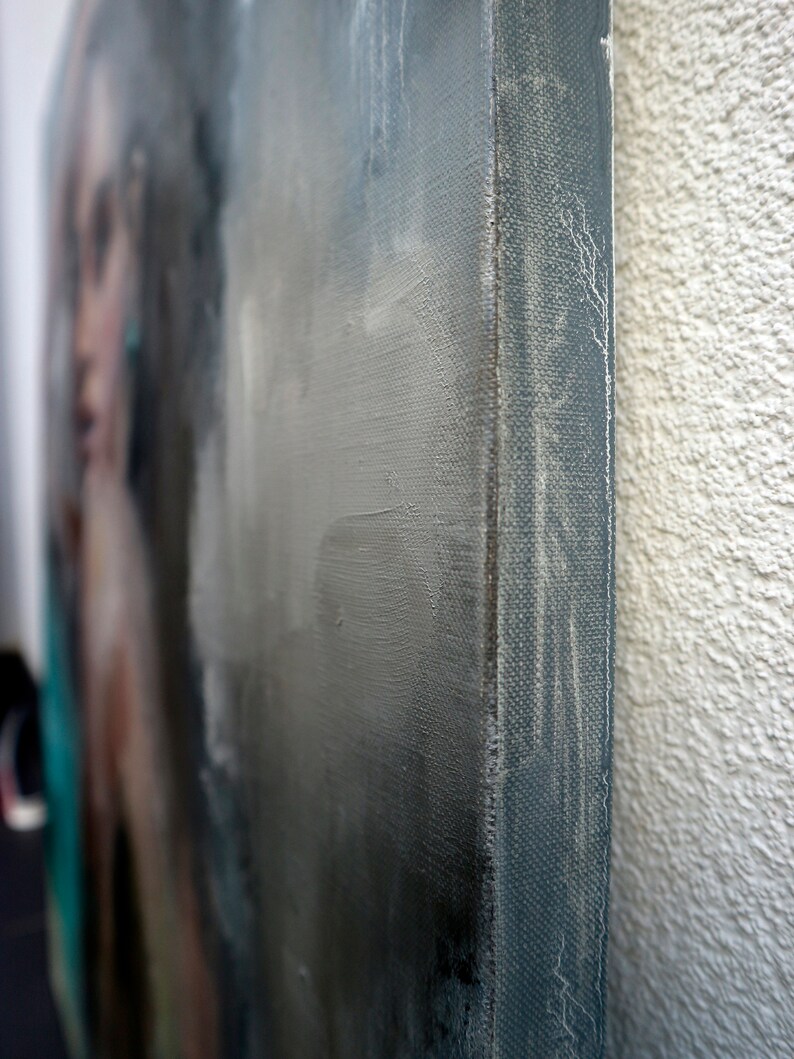 Puede incluir: Primer plano del borde de una pintura sobre lienzo. El lienzo est&aacute; tensado sobre un marco de madera y los bordes est&aacute;n pintados de un color azul gris&aacute;ceo oscuro. El lienzo tiene una superficie texturizada y la pintura se aplica en una capa gruesa.