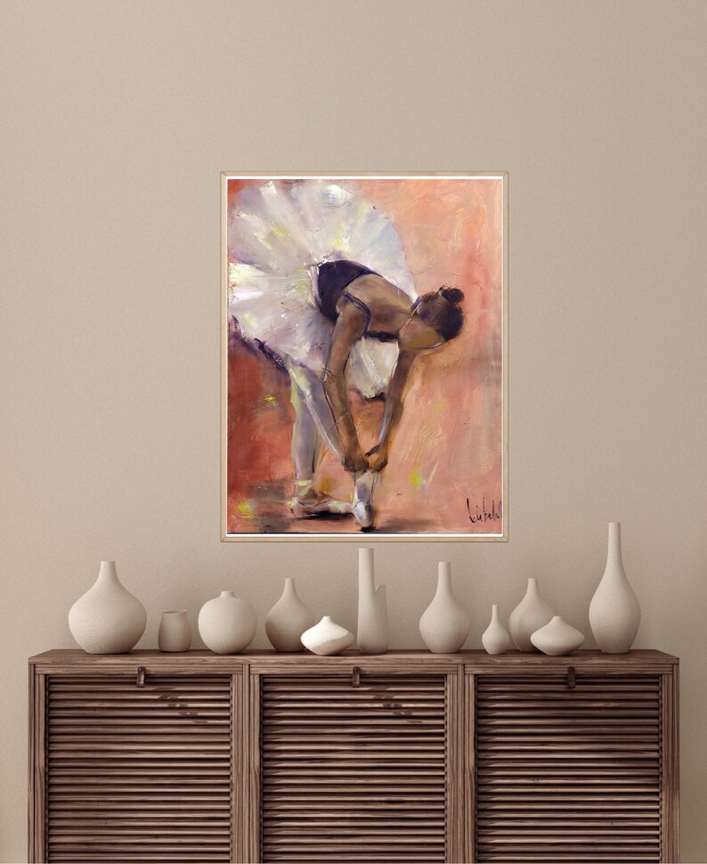 May include: A painting of a ballerina in a white tutu, tying her pointe shoes. The background is a soft peach color with hints of yellow.
