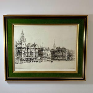 May include: An antique framed print of a detailed architectural drawing, featuring a cityscape with ornate buildings and a central plaza. The print is in a gold frame with a green velvet matting.