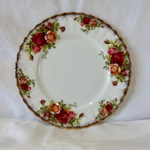 以下が含まれることがあります： 白いセラミックプレート、スカラップエッジと金色の縁。 プレートは赤と黄色のバラと緑の葉で飾られています。 食べ物を提供するクラシックなフローラルデザイン。
