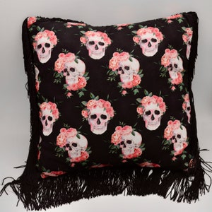 May include: Black throw pillow with a fringe border featuring a repeating pattern of pink flowers and white skulls.