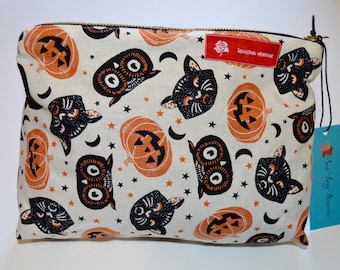 May include: A white zippered pouch with a black and orange Halloween print featuring pumpkins, cats, and owls. The pouch has a black zipper and a red tag with the text "Sewing Machine".