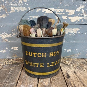 May include: A white ceramic mug with a black handle and the text "But First, Coffee" in a bold, black font. The mug is set against a blurred background, suggesting a cozy setting.