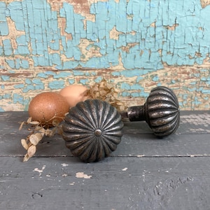 May include: Two antique silver door knobs with a fluted design. The knobs are sitting on a gray wooden surface with brown eggs and dried foliage.