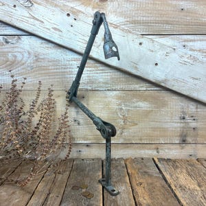 May include: A vintage industrial articulated metal lamp arm featuring a weathered dark gray finish, multiple adjustable pivot joints, and a hollow conical socket at the top end, designed for mounting to a flat surface with a base plate.
