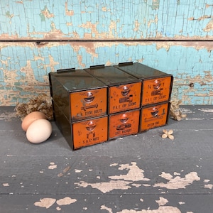 May include: A set of six vintage metal drawers with orange labels. The labels are labeled with different types of screws and bolts, including "1/4" SAE Cap Screws", "1/2" Stove Bolts", "SAE Nuts", "Lock Washers", "Cotton Pins", and "2 1/2" Cap Screws".