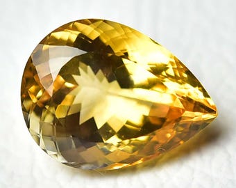 May include: A faceted, pear-shaped gemstone with a warm yellow and amber color. The gem has a brilliant cut, reflecting light across its many facets. The stone is set against a white background.
