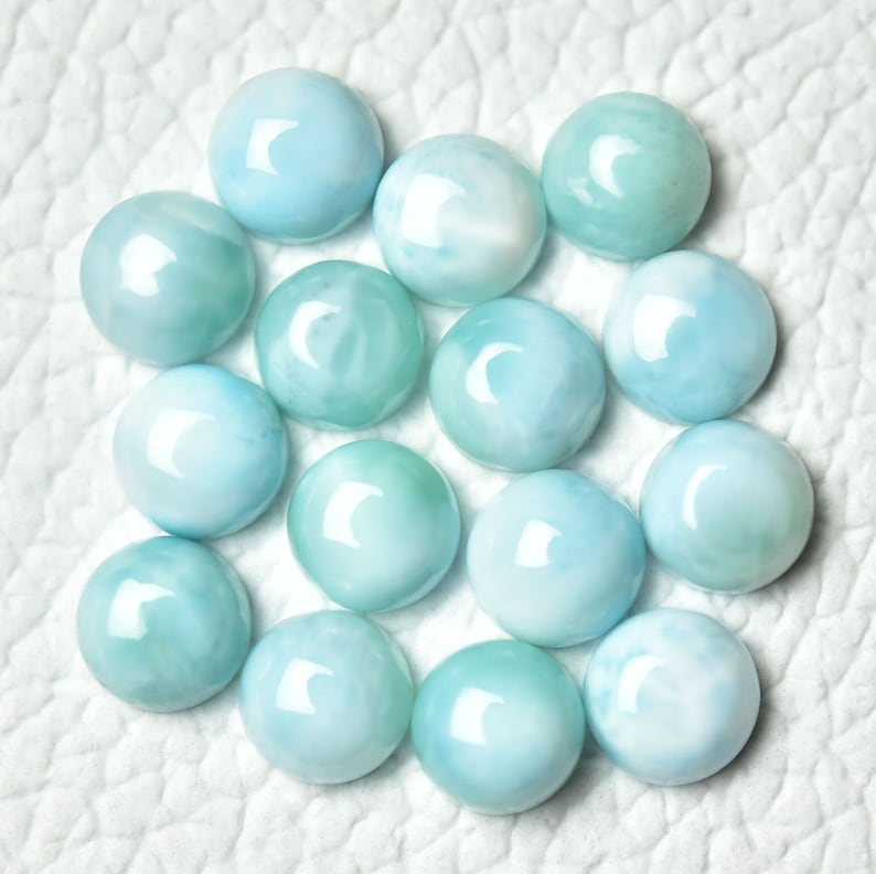 May include: A collection of 15 round, light blue and white cabochon gemstones. The gemstones have a swirling, marbled pattern.
