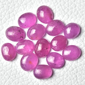 May include: A collection of 13 oval-shaped pink gemstones. The gemstones are smooth and polished, with a slight sparkle.