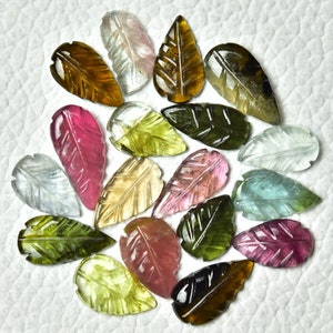 May include: A collection of 18 carved gemstone leaf pendants in various colors, including green, pink, brown, and clear. The leaves are all carved with a detailed leaf pattern.