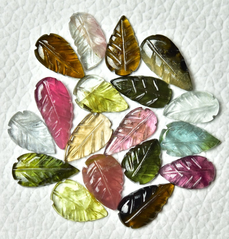 May include: A collection of 18 carved gemstone leaf pendants in various colors, including green, pink, brown, and clear. The leaves are all carved with a detailed leaf pattern.