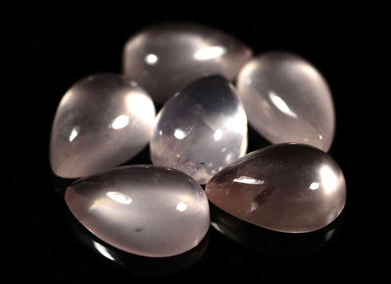 May include: A group of six teardrop-shaped, translucent, light pink gemstone cabochons. The stones are smooth and polished, with a slight sheen.
