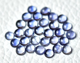 May include: A collection of round, smooth, purple gemstones. The gemstones are arranged in a loose pile on a white surface.