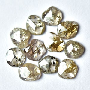 May include: A collection of 10 rough, unpolished, natural diamonds. The diamonds are a light brown color with a slightly gray hue. They are all different shapes and sizes, but they are all faceted.