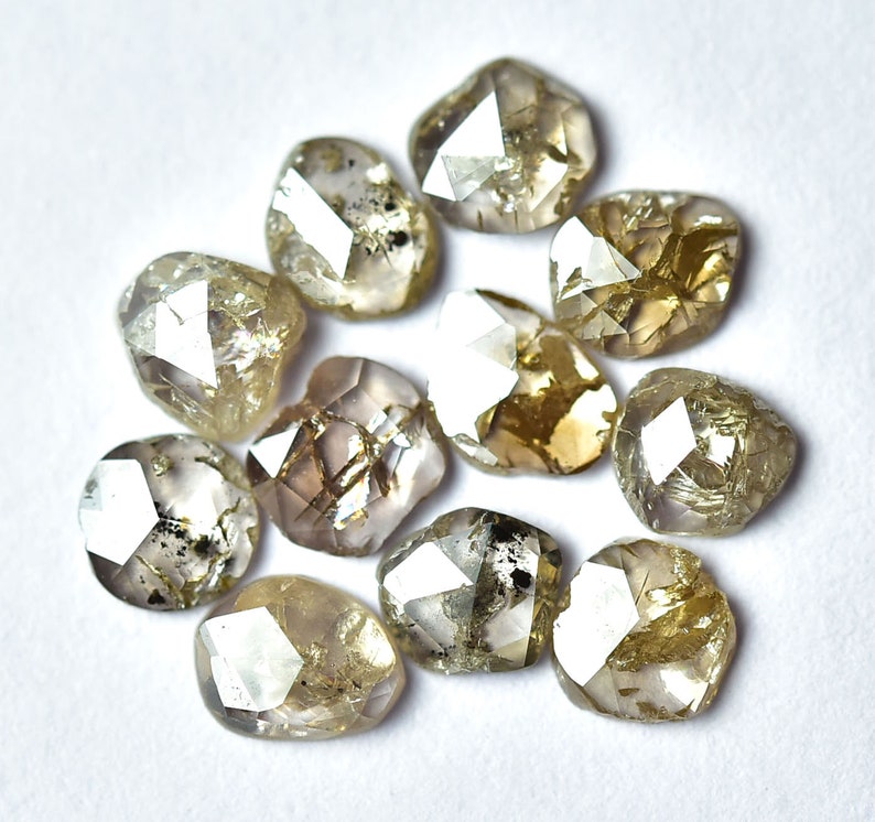 May include: A collection of 10 rough, unpolished, natural diamonds. The diamonds are a light brown color with a slightly gray hue. They are all different shapes and sizes, but they are all faceted.