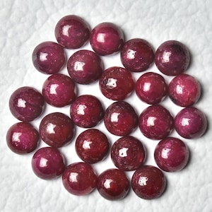 Könnte beinhalten: Eine Sammlung von 25 runden, roten Rubin-Cabochons. Die Cabochons sind glatt und poliert, mit einer leichten Variation in Größe und Form.