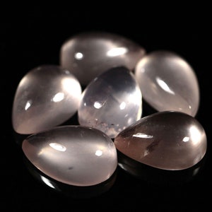 May include: A group of six teardrop-shaped, translucent, light pink gemstones. The stones are smooth and polished, with a slight shimmer.