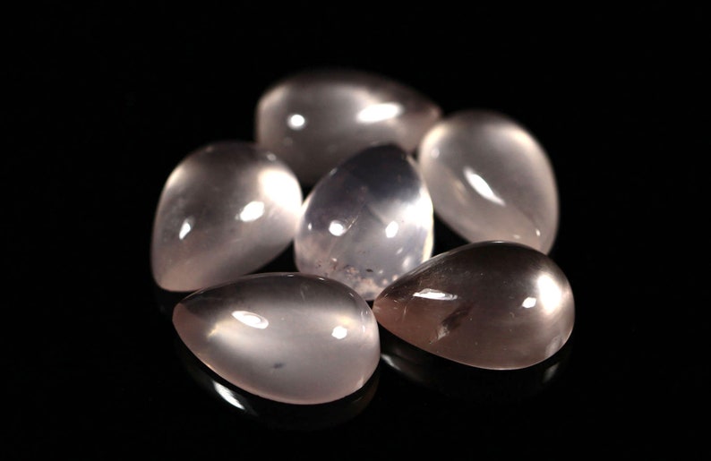 May include: A group of six teardrop-shaped, translucent, light pink gemstones. The stones are smooth and polished, with a slight shimmer.