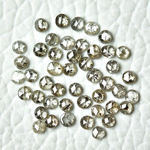 May include: A collection of 30 round, faceted, grey diamonds with a rough, natural finish. The diamonds are scattered on a white surface.