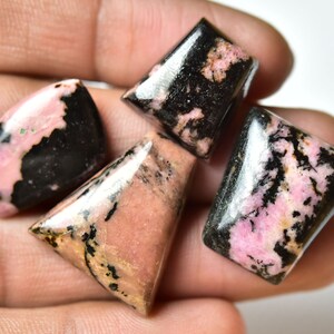May include: Four pink and black gemstone cabochons, cut in different shapes, with a polished finish. The stones have a unique pattern of black and pink.