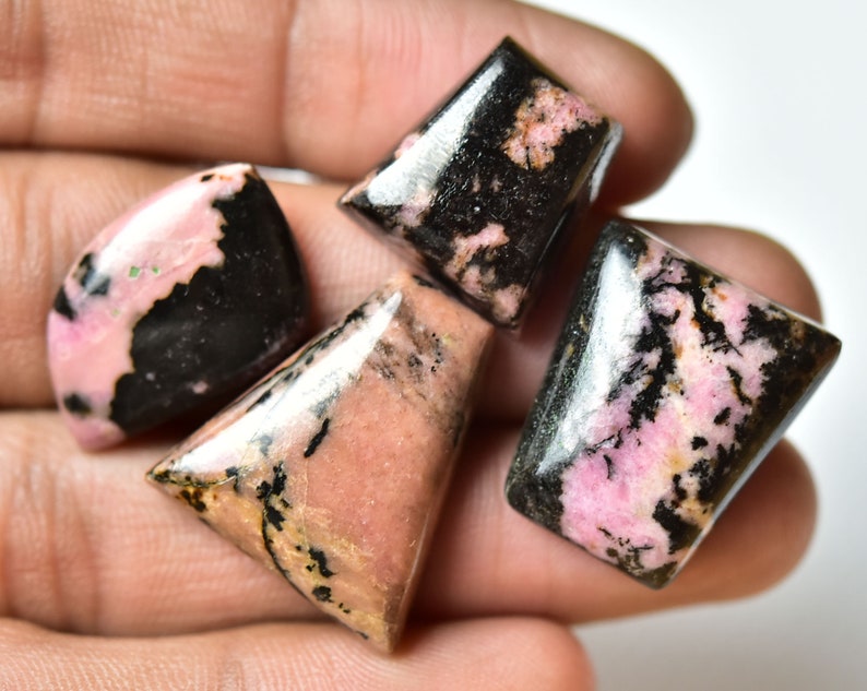 May include: Four pink and black gemstone cabochons, cut in different shapes, with a polished finish. The stones have a unique pattern of black and pink.
