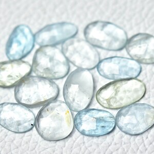 Puede incluir: Una colecci&oacute;n de piedras preciosas de aguamarina azul claro, cada una con una forma ovalada facetada. Las piedras est&aacute;n dispuestas sobre una superficie blanca.