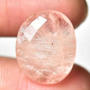 May include: A round, faceted, pink gemstone with a translucent appearance. The gemstone has a slightly cloudy, milky quality.
