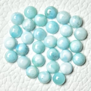 May include: A collection of 25 round, light blue and white cabochon gemstones. The gemstones have a smooth, polished surface and are arranged in a heart shape.