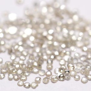 May include: A close-up of a pile of small, white, rough-cut diamonds. The diamonds are scattered on a white surface.