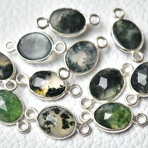 May include: A collection of oval-shaped gemstone connectors with silver-colored settings. The gemstones display a variety of green and white patterns, resembling landscapes. Each connector has a loop on either end for attachment, ideal for jewelry making.