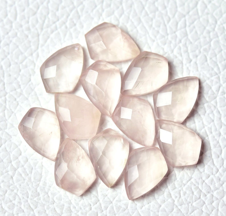 May include: A collection of 12 faceted rose quartz gemstone beads in a pale pink color. The beads are shaped like teardrops and have a smooth, polished finish.