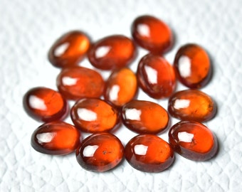 May include: A collection of 14 oval-shaped, orange-red gemstones. The gemstones are smooth and polished, with a glossy finish.