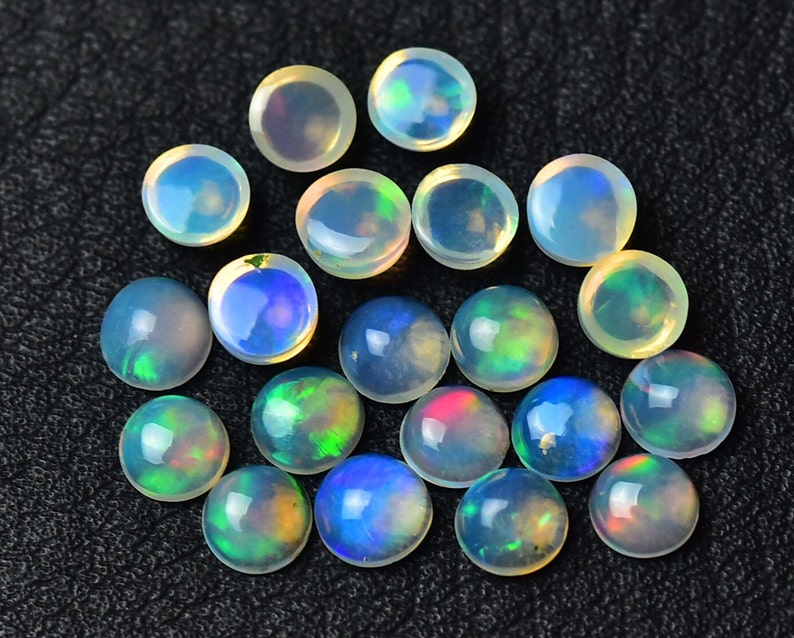 May include: A collection of 17 round, iridescent opal cabochons in various shades of white, blue, green, and pink. The cabochons are approximately 6mm in diameter and have a smooth, polished surface.