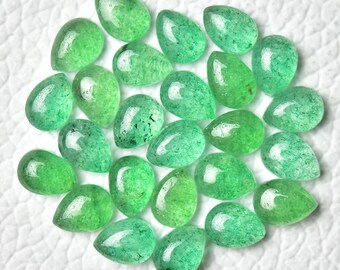 May include: A collection of twenty-one green teardrop-shaped gemstones. The stones vary in shades of green, from light to deep, with a polished, glossy finish. The gemstones are arranged on a white, textured surface.