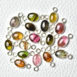 May include: A collection of oval-shaped gemstone charms with silver jump rings. The gemstones are in various colors, including green, pink, brown, and clear.