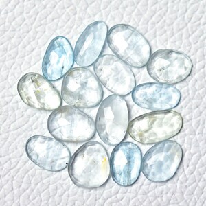 Puede incluir: Una colecci&oacute;n de 14 piedras preciosas de aguamarina facetadas en varios tonos de azul claro. Las piedras tienen forma ovalada y un acabado liso y pulido.