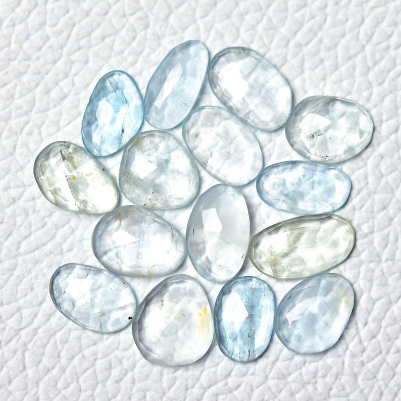 Puede incluir: Una colecci&oacute;n de 14 piedras preciosas de aguamarina facetadas en varios tonos de azul claro. Las piedras tienen forma ovalada y un acabado liso y pulido.