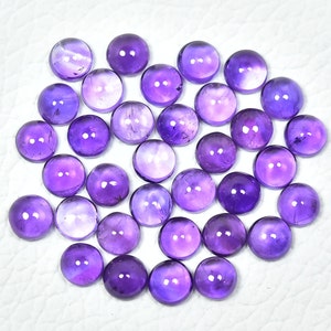 May include: A collection of 35 round, purple amethyst cabochons. The cabochons are smooth and polished, with a slight variation in color and size.