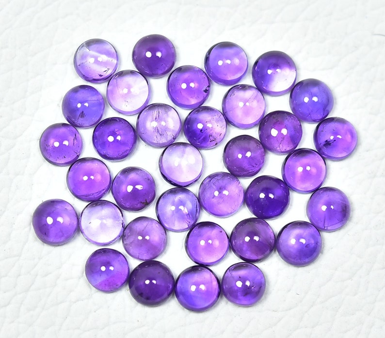 May include: A collection of 35 round, purple amethyst cabochons. The cabochons are smooth and polished, with a slight variation in color and size.