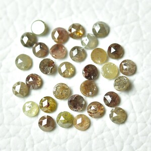 Op de afbeelding: Een verzameling van meer dan 20 ruwe, ongeslepen, ruwe diamanten in verschillende tinten bruin, groen en geel. De diamanten zijn rond en hebben een gefacetteerde, gepolijste afwerking.