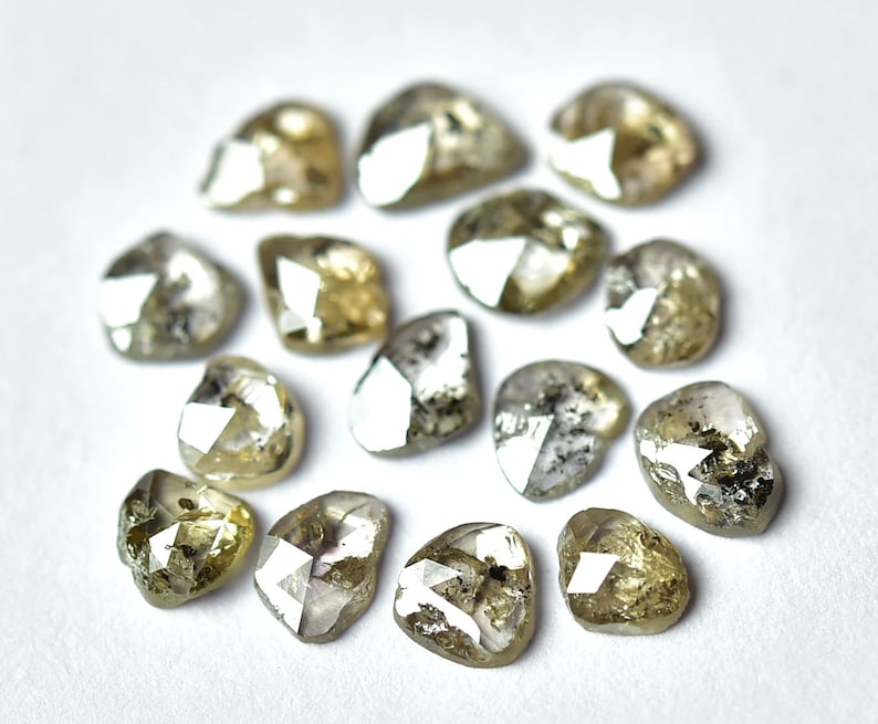 May include: A collection of rough, unpolished diamonds in various shades of gray and brown. The diamonds are heart-shaped and have a natural, raw appearance.