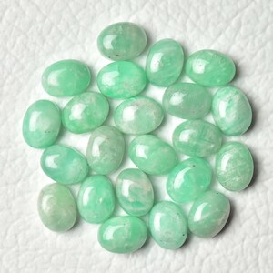 Peut inclure: Une collection de 18 pierres pr&eacute;cieuses vertes de forme ovale, probablement de l'amazonite, dispos&eacute;es en cercle sur une surface blanche.