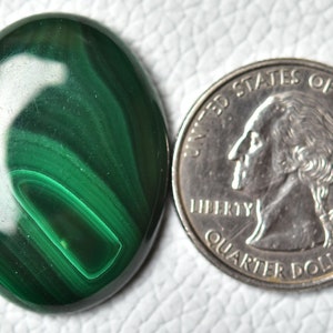 May include: A green malachite cabochon, oval shaped, with a swirling pattern. The cabochon is about the size of a US quarter.